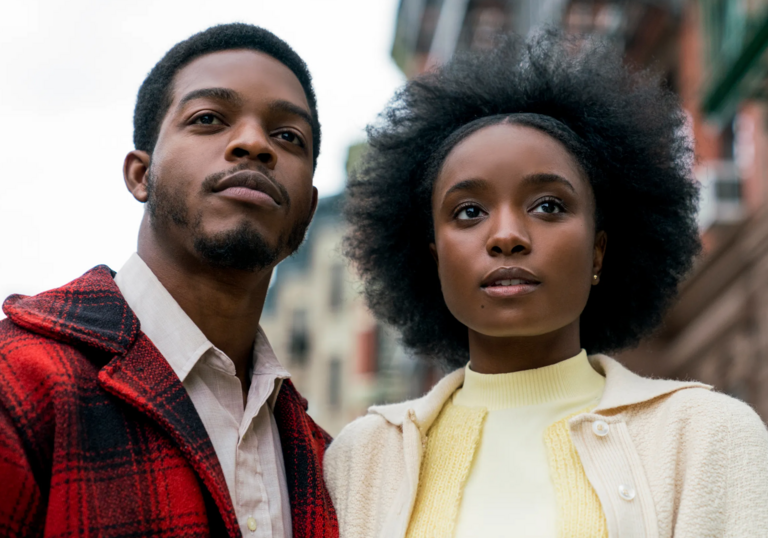 A man and a woman stand in an urban American street, looking forward.