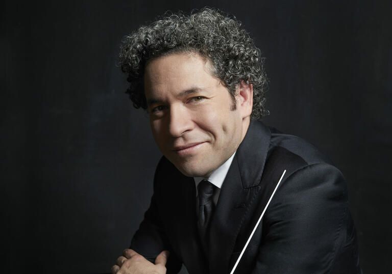 Headshot of Gustavo Dudamel smiling at the camera while holding his baton.