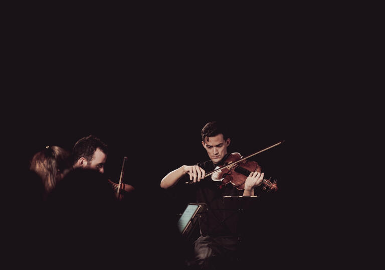 Photo of Stephen Upshaw playing his viola in a darkly lit room