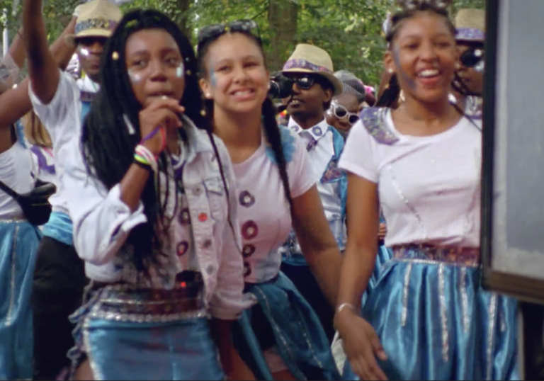 A group of excited young women walk down a street, wearing blue skirts.