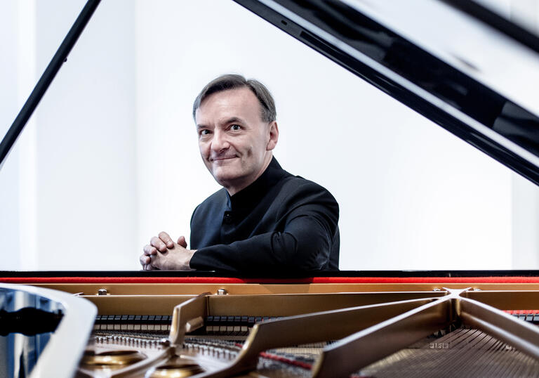 Stephen Hough sitting at a grand piano, smiling at the camera