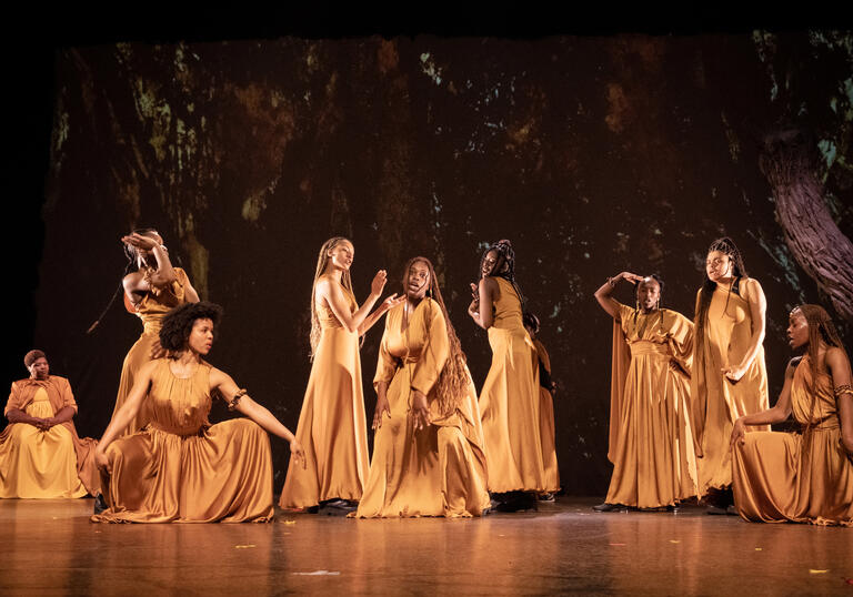 The cast of The Golden Stool performing on stage, wearing long golden dresses