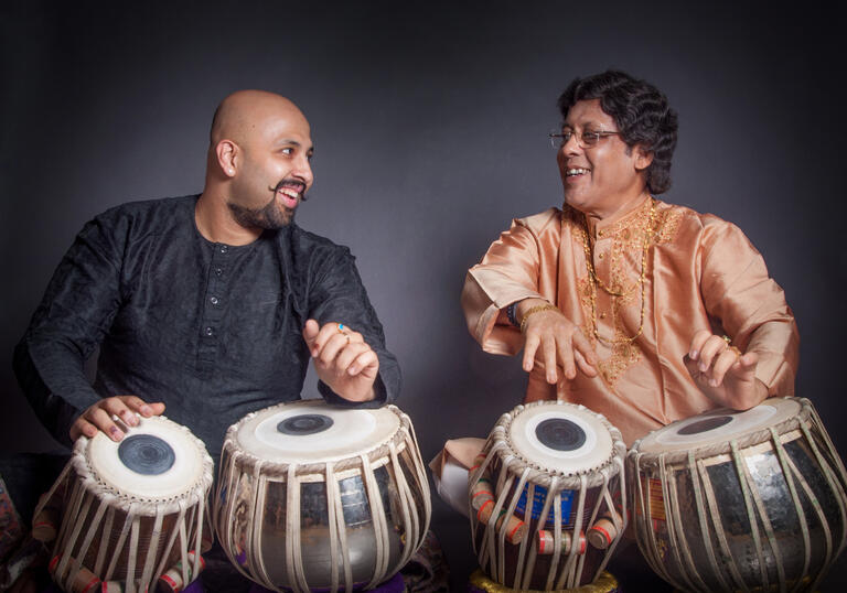 Anindo and Anubratta Chatterjee playing the tabla, smiling at each other