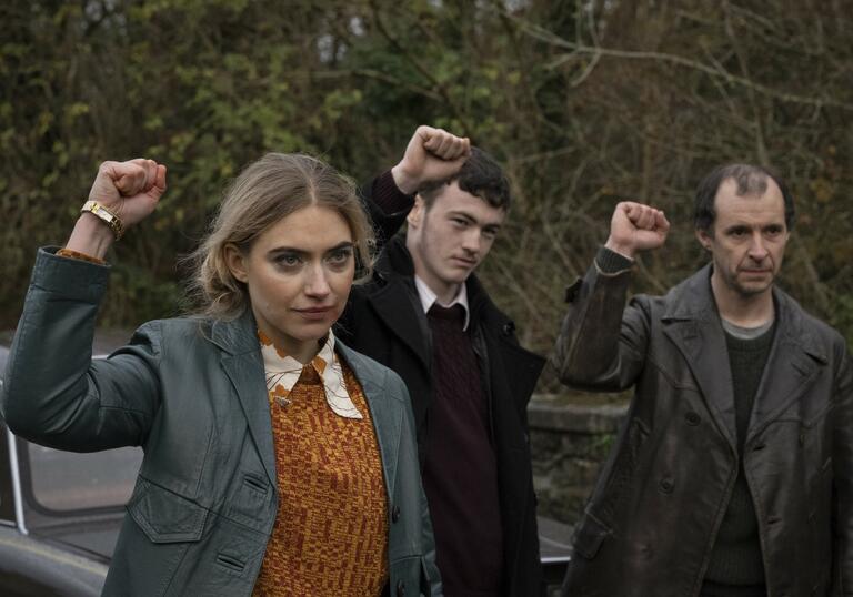 A woman and two men in 60s clothing raise a fist to the sky in defiance or solidarity.