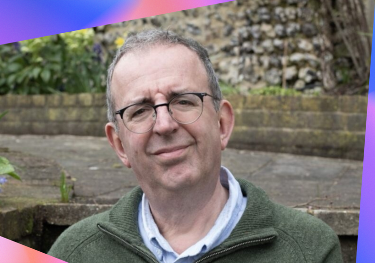 Rev Richard Coles standing in a walled garden, smiling at the camera