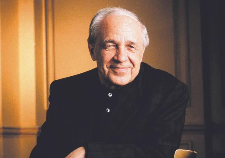 Composer Pierre Boulez sitting down. He is wearing a dark jacket and has white hair.