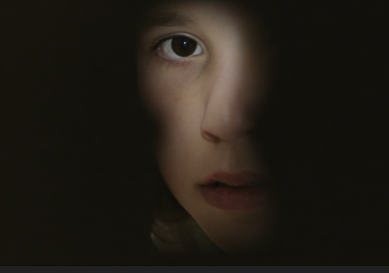 A young girl looks through a key hole.