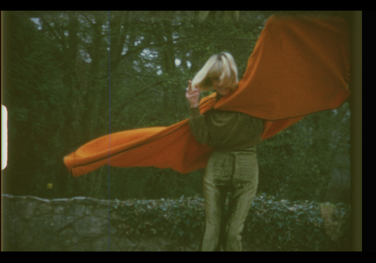 A woman in a large orange cape spins on a roof top.