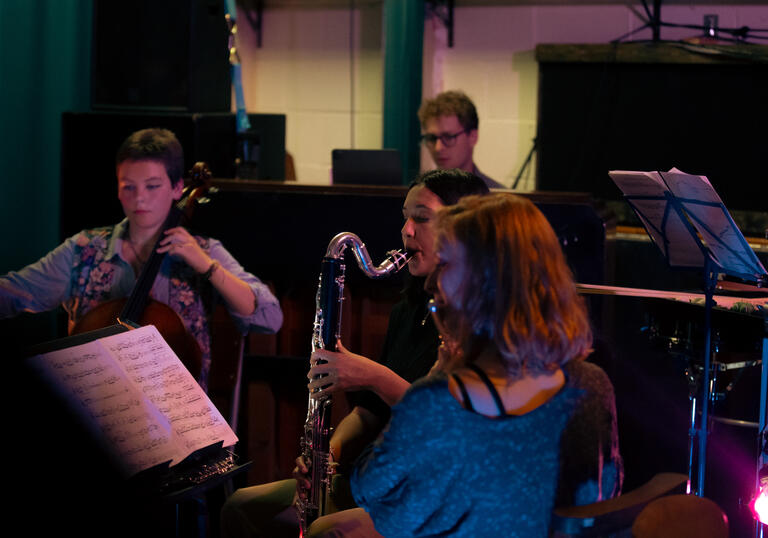 A cellist, bass clarinettist, flautist and pianist sitting playing their instruments