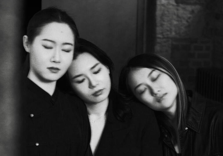 Three members of Tangram stand with eyes shut, heads resting on each other's shoulders