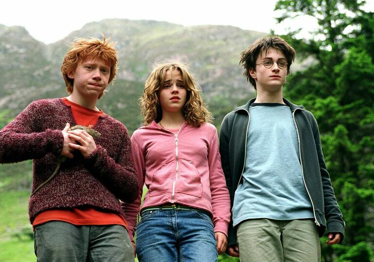 Three young, dishevelled teens stand in a stunning landscape, one holds a rat.