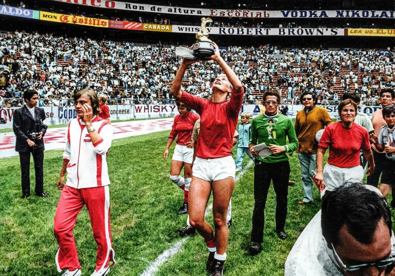 A group of women footballers celebrate in a huge stadium, holding an award cup.