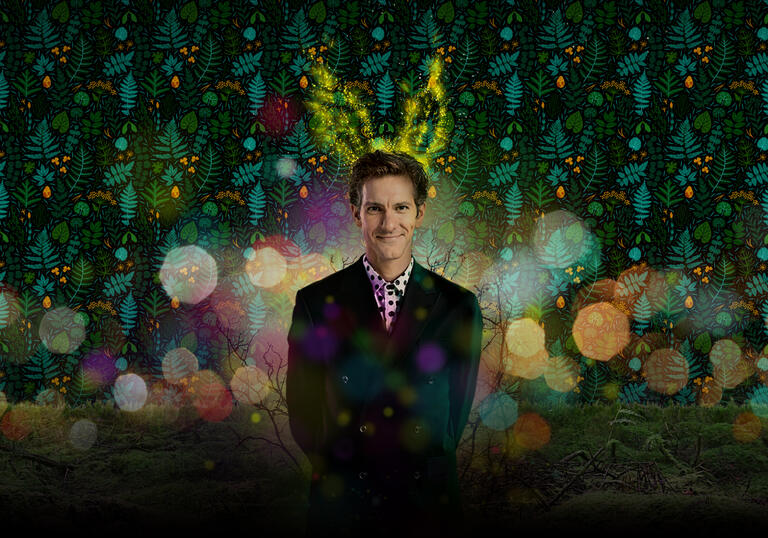 A person in a suit has a pair of glowing antlers above their head while standing against a red and green background.