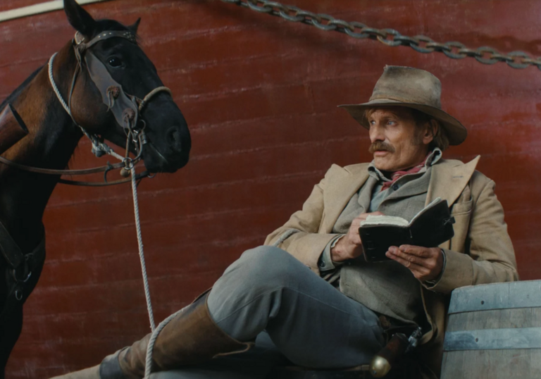 A man is sitting next to a horse in front of a brand.