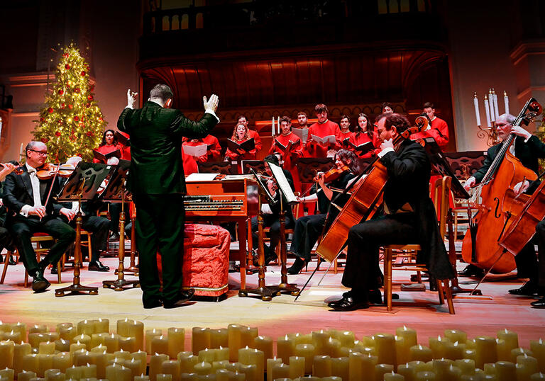 The orchestra performing on stage, surrounded by candles and two Christmas trees