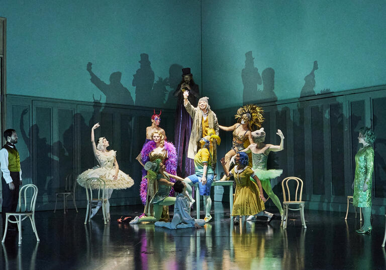 A group of ballet dancers in very colourful clothing pose on a turquoise stage.