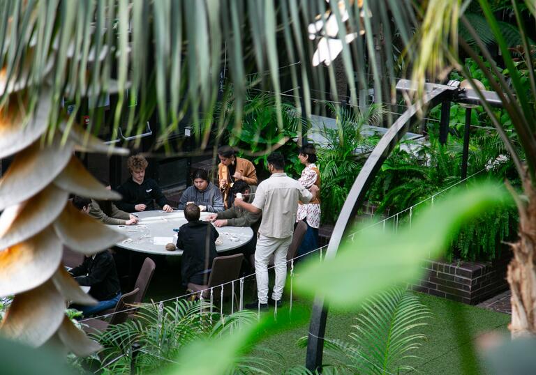 Group of secondary school children crafting around a table in the conservatory, surrounded by plants