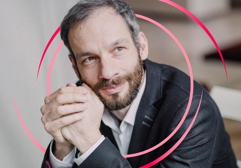 Dima Slobodeniouk clasping his hands in front of his face, with pink circular swirls around him
