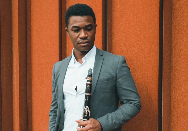 Carlos Ferreira standing with his clarinet against an orange wall