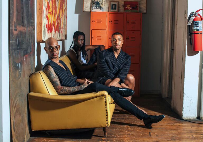 Davóne Tines, Khari Lucas and John Bitoy sitting on a yellow sofa