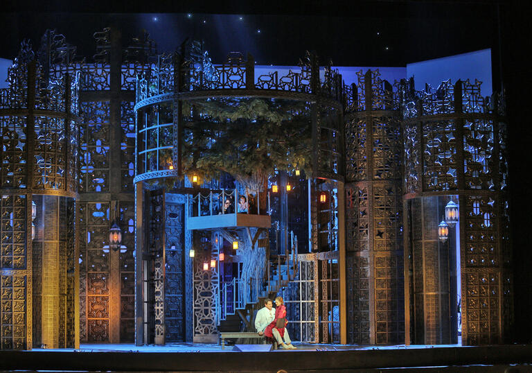 Young lovers sit together in the garden of a beautiful estate, in a theatre production.