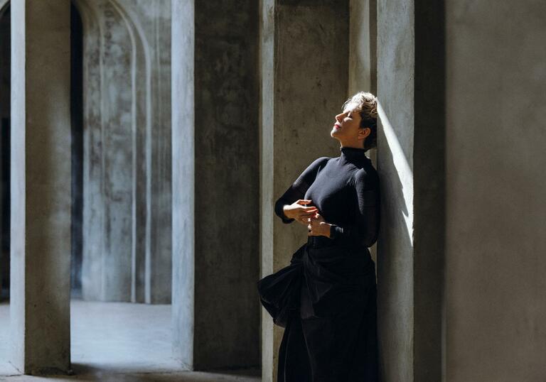 Joyce DiDonato in a black dress, leaning with her back against a wall