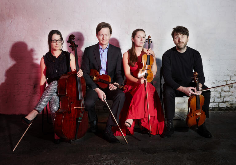 The Ligeti Quartet sitting in a row, holding their instruments
