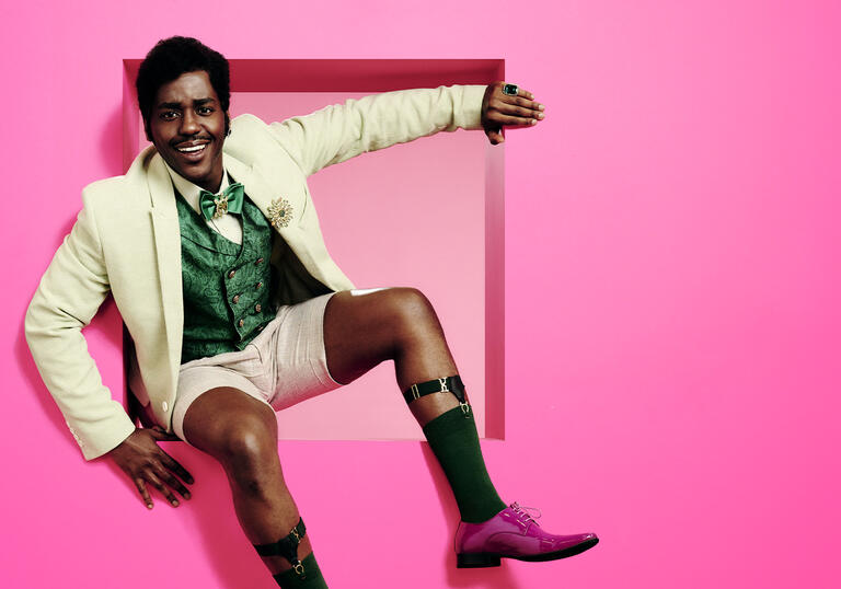 A man in 1800s clothes sits in a bright pink square.