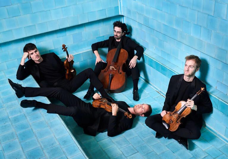The four members of Quatuor Agate in black suits, sitting in various positions in an empty swimming pool, holding their instruments