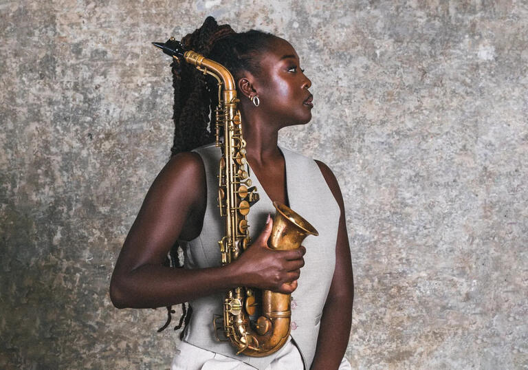 A profile shot of Cassie Kinoshi holding her saxophone in front of a concrete wall