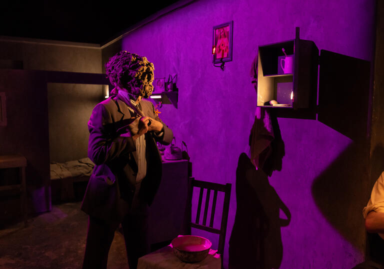 A person in a suit wearing a clay mask gets dressed.