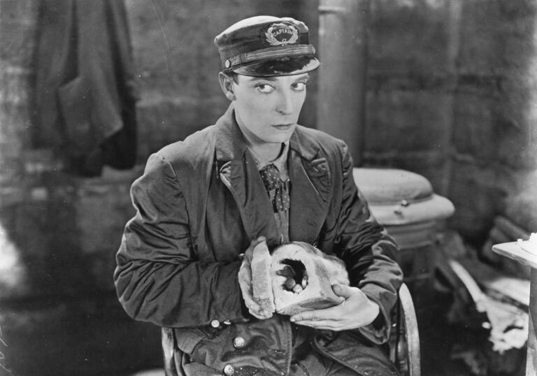 A black and white image of a man dressed in a cap and holding a hollowed out loaf of bread.