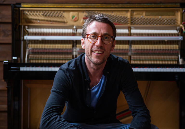 Bill Laurance smiling at camera with upright piano in the background