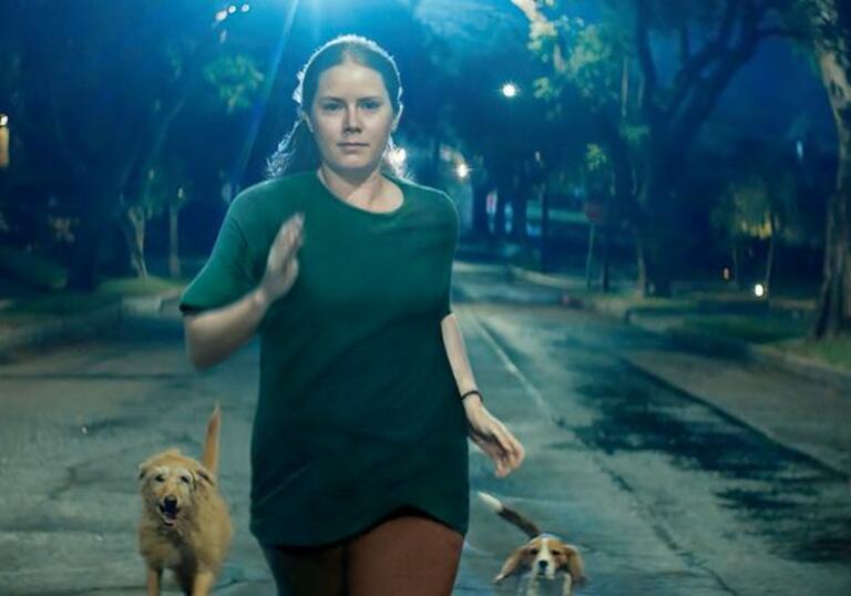 Amy Adams runs down a dark street, surrounded by dogs