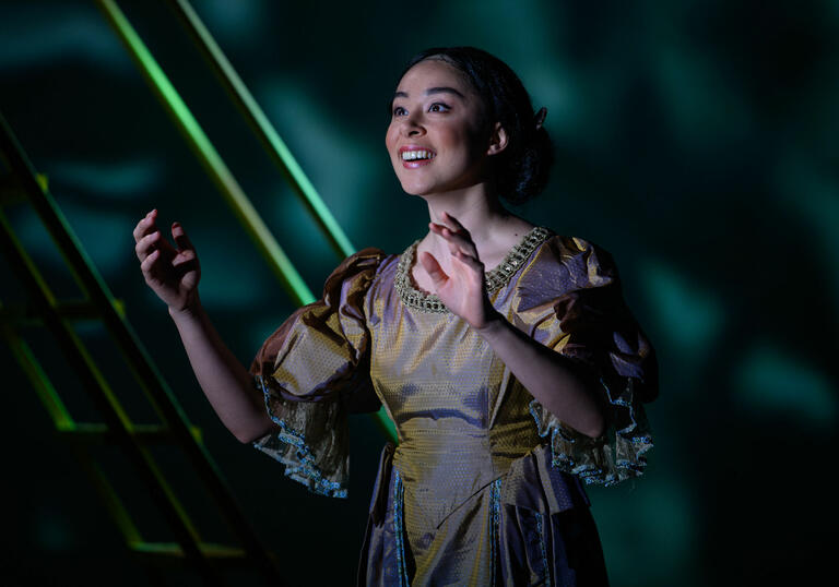 Guildhall School opera singer with arms raised, smiling against a green background