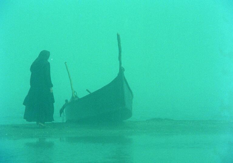 A misty scene with a bright green tint, showing a woman standing next to a moored boat.