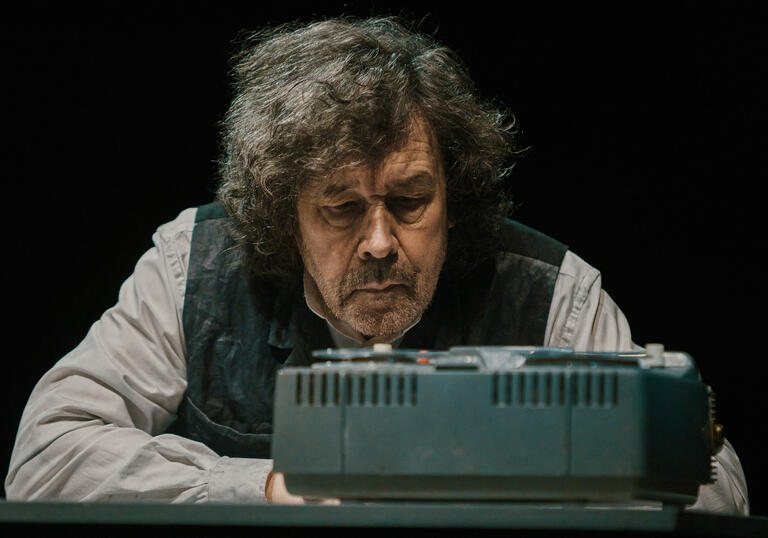 Actor Stephen Rea sits in front of a tape machine.
