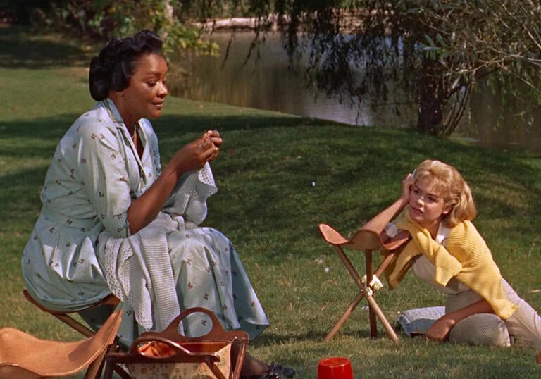 An older woman sits on the grass with a younger woman at her feet.