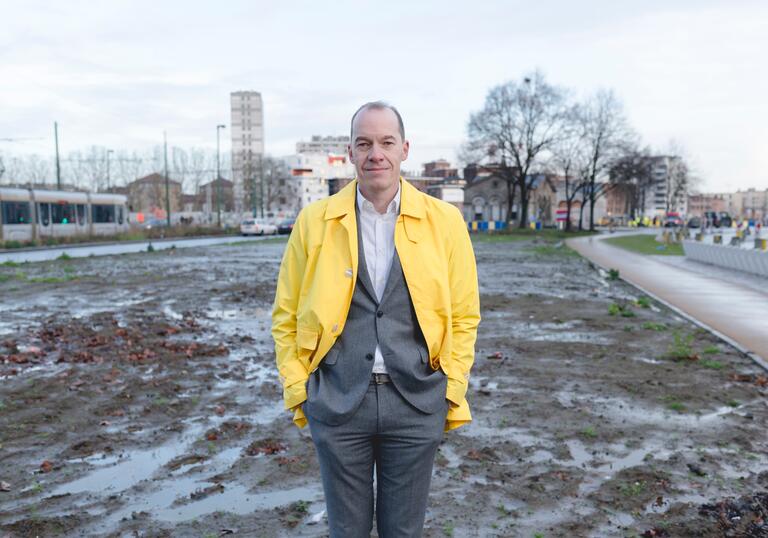Kristiaan Borret standing on a waterlogged building site, wearing a bright yellow jacket.