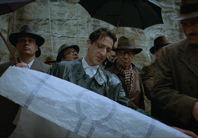 A man hold a map in the rain as others with umbrellas look at it.