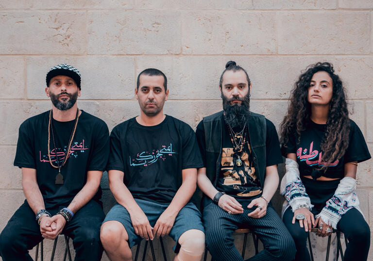 A portrait of band DAM, three men and a woman dressed casually in black t-shirts and denim and looking into the camera