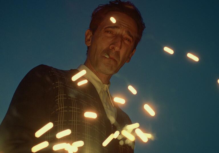 Adrien Brody stares down into camera, smoking