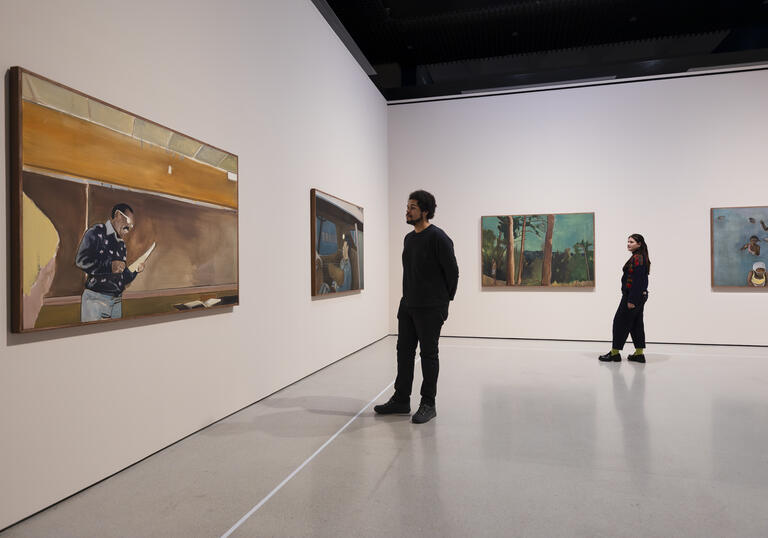 Four of Noah Davis's paintings hanging on white walls. Two people stand between the paintings, looking at them.