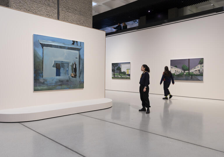 Three of Noah Davis's paintings hanging on white walls. Two people are looking at the paintings.