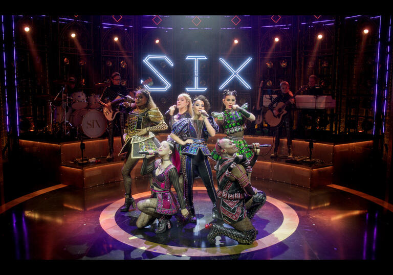 The queens perform on the stage with the band behind them.
