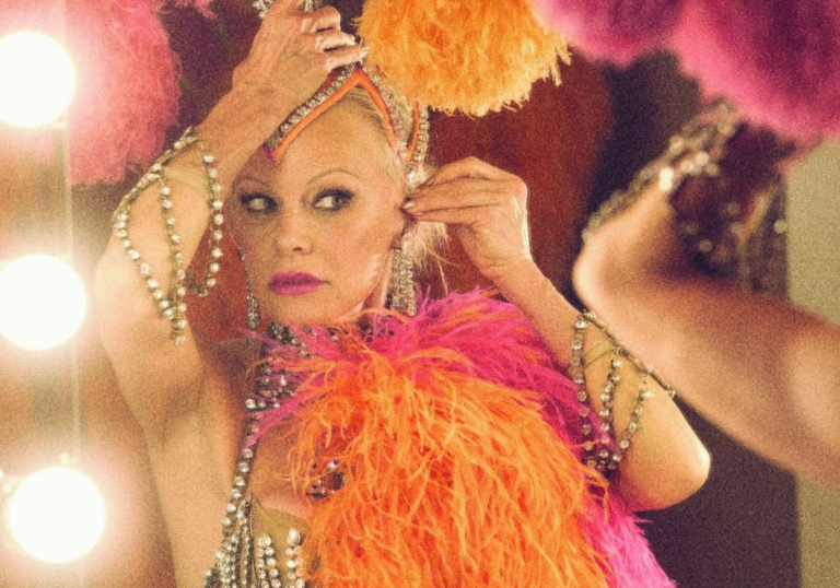Pamela Anderson adjusts her pink and orange Las Vegas headdress in a mirror