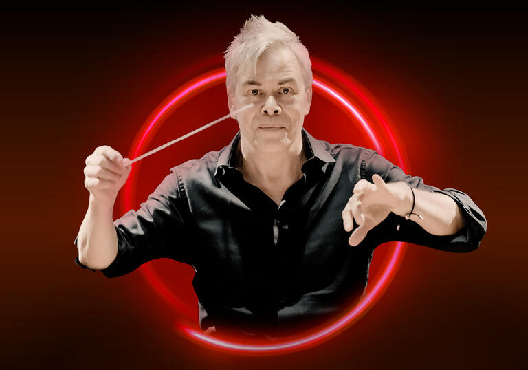 Hannu Lintu with his arms raised against a red bakcground