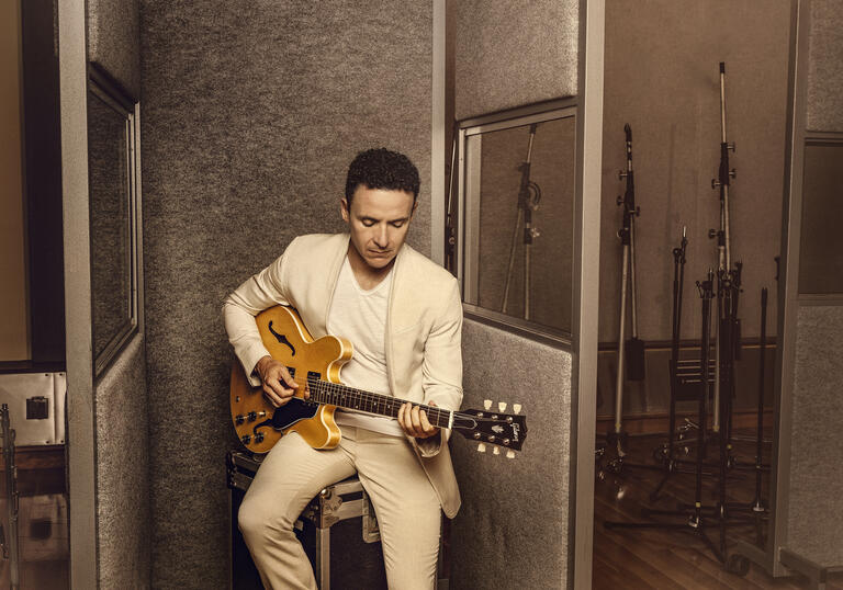Image of Fonseca in a white suit sat down playing the guitar.
