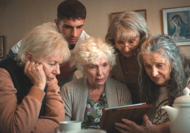 Four mothers and a young man sit around an iPad
