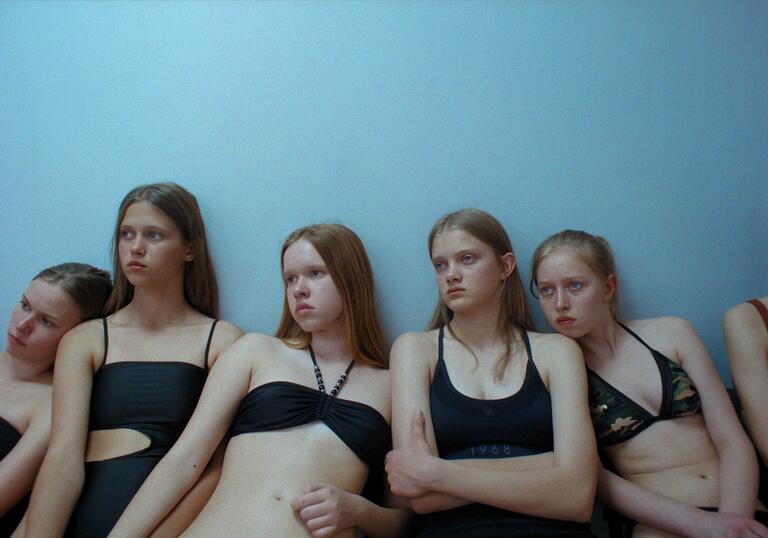 A group of young girls wearing black swimming costumes stare despondently